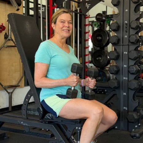 Woman performing seated dumbbell curls on a bench at Real Fitness